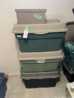 Stack of three Rubbermaid hinged top totes in dark green, light green, and gray, with a small gray decorative box on top.