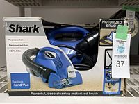 Blue Shark handheld vacuum cleaner in original box showing front with motorized pet hair brush and hose attachment.