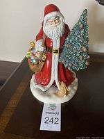 Full front view of the hand-painted Father Christmas figurine showing red robe, tree, toy bag and rabbit at base.