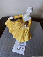 Full view of the Royal Doulton figurine Kristy showing the yellow dress and pose with one hand holding the dress and the other extended forward.