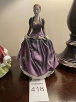 Full view of the Royal Doulton figurine "Victoria" showing the entire figure dressed in a glossy purple gown with gold detail.