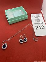 Full set necklace and earrings displayed on red fabric next to mint green jewelry box and auction lot card.
