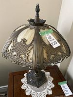 Full view of antique slag glass table lamp on wooden surface with doily underneath, showing ornate metal frame and glass shade.