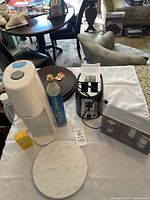White SodaStream machine with gas cylinder, Black+Decker toaster, faux marble lazy susan, Salt & Pepper mills, and placemats laid out on white cloth