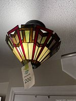 Close-up image of one stained glass flushmount fixture installed on ceiling, showing geometric red, amber, cream, and brown design and bronze finish base.