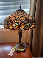 Tiffany style stained glass lamp with colorful intricate stained glass mosaic shade placed on a wooden surface near window.
