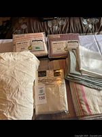 View of multiple folded sheets and blankets, including new packaged and unpackaged microfiber fitted sheets, pink and purple striped flannel blankets, and extra pillowcases.
