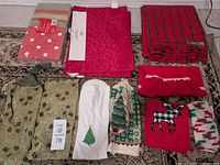 Photo shows various Christmas-themed linens including a half apron, hand towels, cloth napkins, and placemats laid out on a carpet.