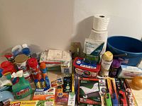 Photo showing assortment of household cleaning products, paper towels, bucket, and related items.