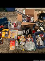 Wide view showing all items laid out including tools, light bulbs, tapes, boxes, and containers on a patterned carpet
