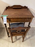 Front view of the vintage wooden writing table and chair showing decorative carved edge on table, single drawer, and spindled chair with padded striped cushion.
