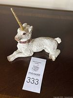 Full view of the white unicorn figurine lying down with a gold horn, pink jeweled collar, and detailed texture.