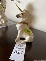 Front and side views of the sitting unicorn figurine showing the golden horn and gold chain around its neck.