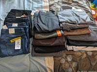 Photo showing a variety of folded and stacked women's pants including denim with tags, formal and casual styles in multiple colors and patterns.