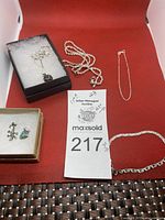 Overall lot shot showing all jewelry items arranged on red surface: thick chain missing ring, two bracelets, necklaces, and two pendants.