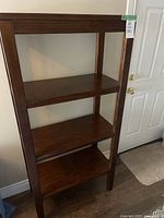 Full view of the wooden open shelving unit with three shelves and dark finish.