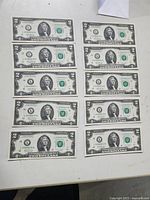Front side of ten sequential US two-dollar bills laid out in two columns of five on a white surface.