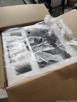Unopened 3D printer components packed in molded foam inside cardboard box with plastic wrapping.