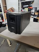 Front-right angled view of the APC Smart-UPS 1500 unit on a table in a warehouse setting.