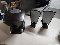 View of black Benwin subwoofer with rounded top grille and front port, positioned next to two satellite speakers on table