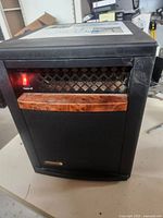 Front side view of EdenPURE portable heater showing the heating element lit, wood accent panel, and brand plaque.