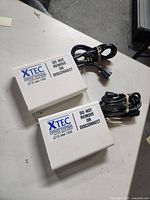 Top view of two white rectangular XTEC Office Systems power tap and surge protectors with cords tied in rubber bands on a light surface