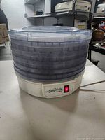 Front view of the Mr. Coffee food dehydrator showing the white base with a lighted red power switch and multiple stacked translucent trays with a clear lid.