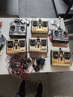 Top-down view of six Futaba RC plane controllers and wiring accessories on table.