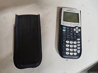 TI-84 Plus graphing calculator next to its black protective sleeve case on a white surface.