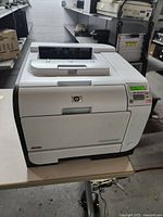 Full view of HP Color LaserJet CP2025 printer on a table, showing its white and gray casing and paper tray.