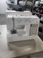 Front view of white Huskystar portable sewing machine on table with hard case behind it.
