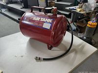 Side view of the red cylindrical portable air tank with carrying handle, pressure gauge, valve, and attached hose lying on a table.