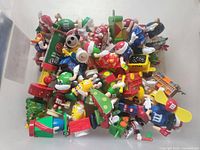 Top-down view showing a jumble of colorful M&M character figurines mostly in Christmas attire, toy train parts, and small holiday-themed accessories.