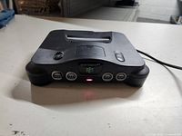Front view of the black Nintendo 64 console powered on with red light indicator, showing four controller ports and cartridge slot.