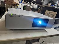 Front view of the Panasonic F100 projector powered on with lamp light indicator active.