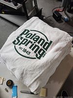 Close-up photo of white towel with green Poland Spring logo and text 'Est. 1845'. Logo circular in design.