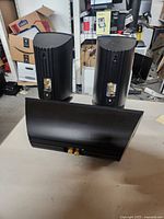 Photo showing front and rear of two black ProCinema bookshelf speakers and one center channel speaker in black finish on a tabletop.