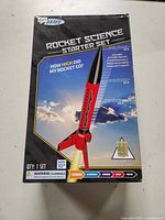 Front of the unopened Estes Rocket Science Starter Set box featuring a red and black rocket with identification and warnings