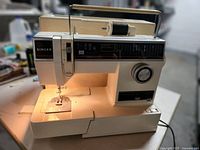 Full view of the Singer portable sewing machine illuminated and threaded with black thread on the spool holder, showing stitch plate and needle area.