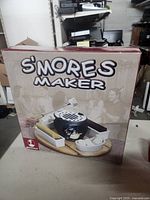 Photo of the front of the product packaging showing the s'mores maker kit with utensils and trays, used for identifying the product and its contents.