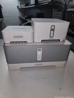 Three Sonos audio devices stacked showing front panels and brand logos.