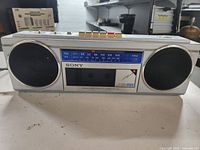 Front view of Sony stereo cassette-corder showing the speakers, cassette tape window, and FM/AM radio tuning scale.