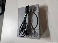 Top view of Sony PlayStation One with power cord placed on top, showing circular disc lid and front buttons.