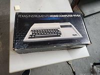 Closed original cardboard box labeled “Texas Instruments Home Computer 99/4A” on table surface