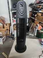Front view of the black tower fan showing vertical grille and control dial at top.