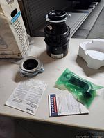 Whirlpool garbage disposal unit with mounting assembly, instructions and discharge pipe on table surface.