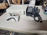 White Xbox 360 console with controller and power supply on table, showing overall lot contents.