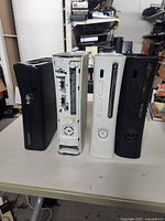 Four Xbox 360 consoles arranged side by side on a table showing front and internal view of one unit
