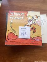 Front cover of book 'Weirdos From Another Planet! A Calvin and Hobbes Collection by Bill Watterson' shown on wooden table.