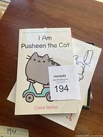 Books laid out with top visible book titled 'I Am Pusheen the Cat' by Claire Belton featuring illustrated cat on scooter cover.